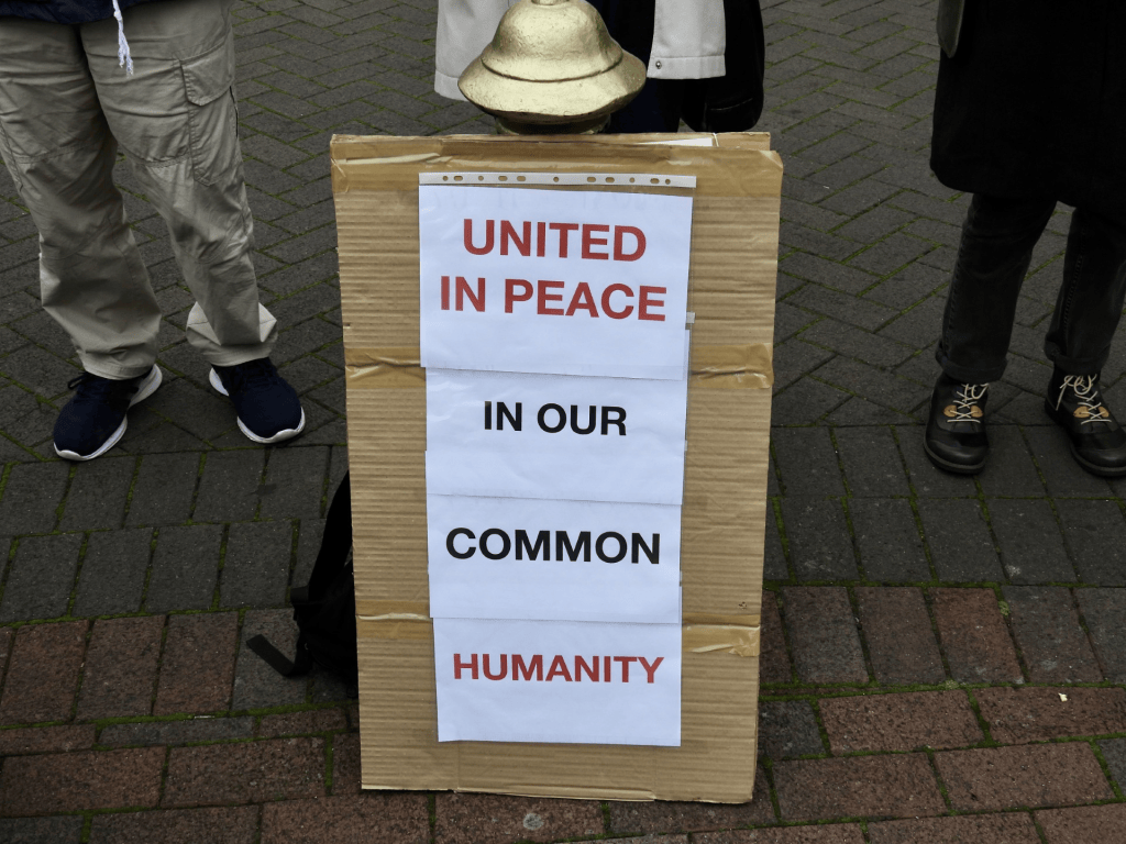 A cardboard sign with the text 'UNITED IN PEACE IN OUR COMMON HUMANITY' displayed on a street during a gathering.